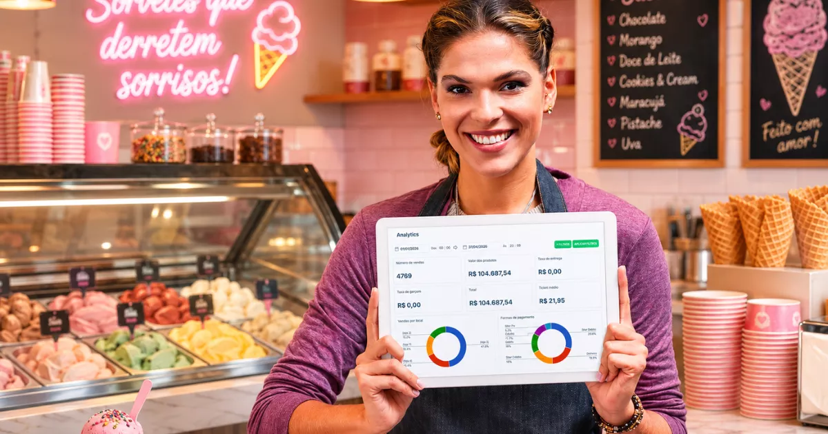 Dona de sorveteria de avental sorrindo segurando tablet com dashboard de analytics, com balcão refrigerado de sorvetes coloridos e cardápio em lousa ao fundo